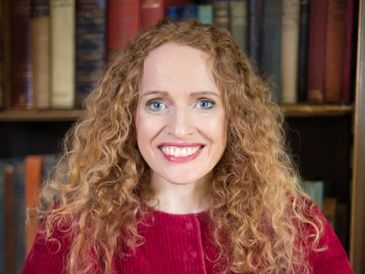 Smiling woman with curly hair in front of bookshelves.