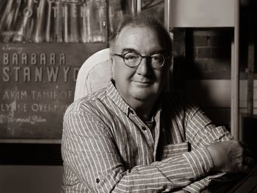 Black and white portrait of a man with glasses smiling.