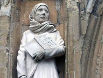 Statue of a woman holding a book titled 'The Holy Bible' in a historic stone setting.