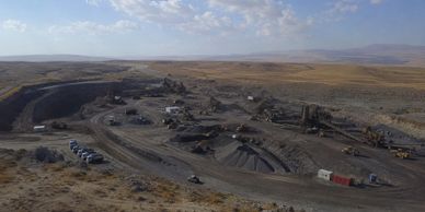A large open-pit mining site in a barren landscape under a partly cloudy sky.