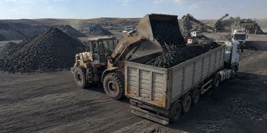 Loader dumping coal into a large truck at a mining site.