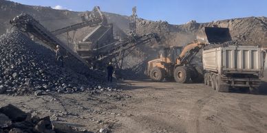 Heavy machinery loading coal onto a truck at a mining site.