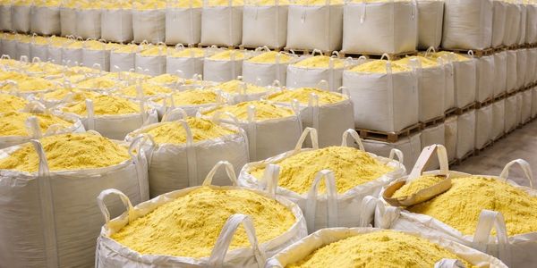 Large white bags filled with yellow powder stacked in a warehouse.