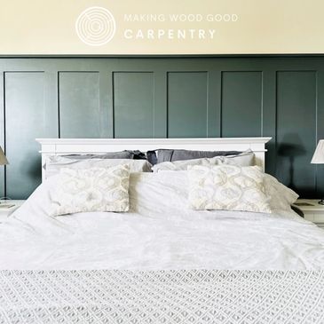 Cozy white bed with decorative pillows against a dark paneled wall.