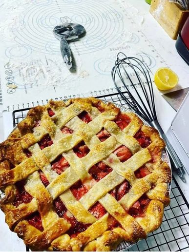 Strawberry rhubarb pie sitting on a cooling rack next to a whisk and a lemon