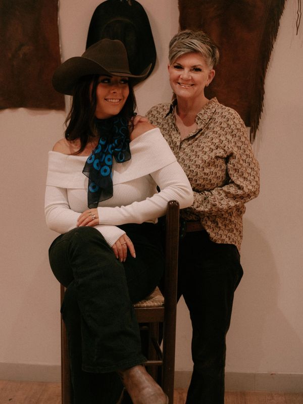 Two women posing indoors with Western-style attire and smiling warmly.