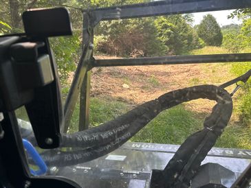 View from inside an off-road vehicle looking out onto a dirt trail through a forested area.