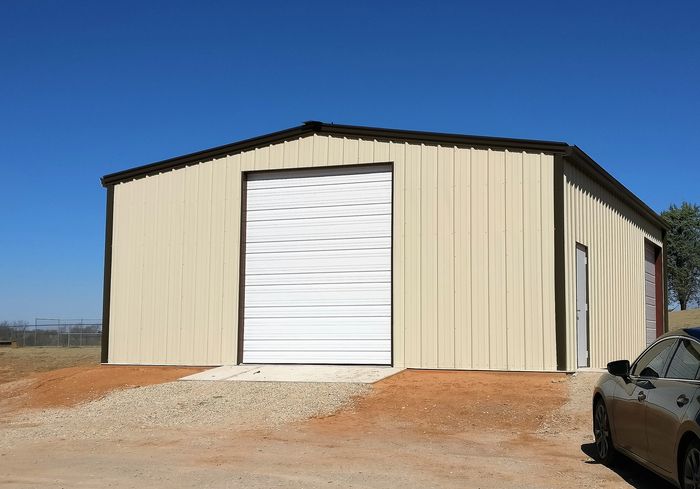 A beige metal storage building with a closed white garage door under a clear blue sky.