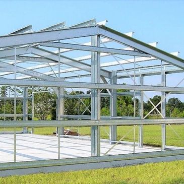 Steel frame structure under construction on a grassy field.