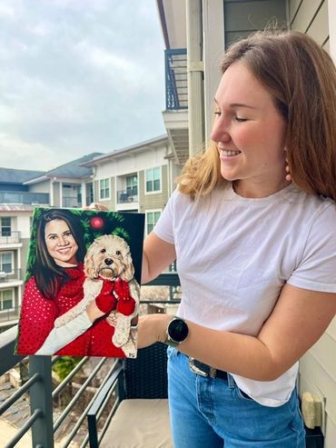 Woman holding a festive portrait of a lady and a dog in holiday attire.