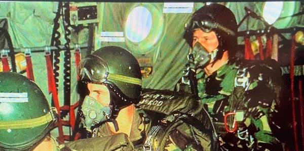 Military personnel in helmets and oxygen masks inside an aircraft.