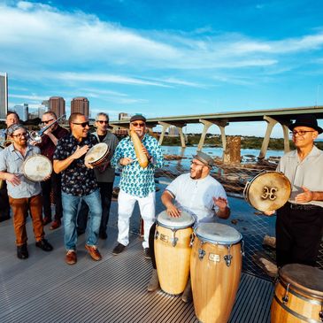 A band playing percussion instruments outdoors near a bridge.