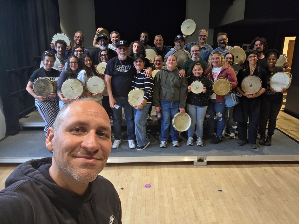 Un grupo diverso sosteniendo tambores sonríe para una selfie.