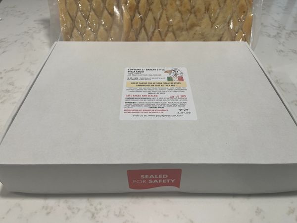 Box of bakery-style pizza crusts sealed for safety on a marble countertop.