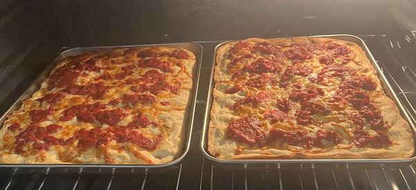 Two rectangular pepperoni pizzas baking in the oven on trays.