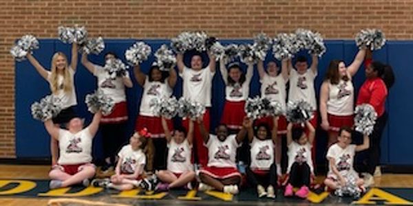 A diverse cheerleading team poses with pom-poms in a gymnasium.