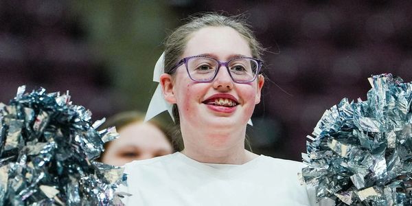 Smiling cheerleader holding silver pom-poms during a performance.