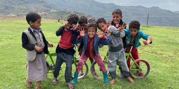 Six joyful boys posing and playing on green grass with a bicycle.