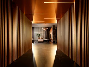 Modern hallway with warm lighting and wooden panel walls leading to a stylish living area.