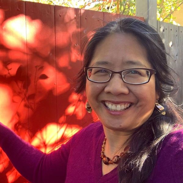 Asian american woman wearing glasses smiling at the camera with beautiful leaf patterns behind her.