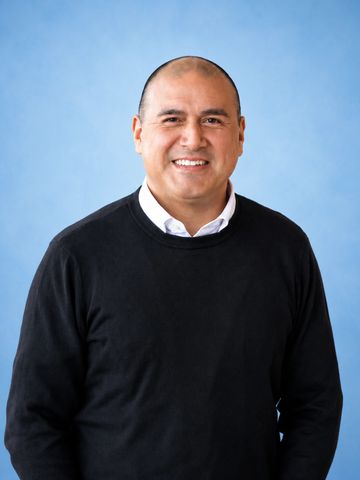 Smiling man in black sweater against blue background.