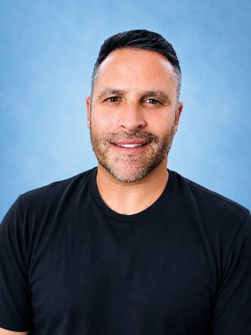 Smiling man in black t-shirt against blue background.