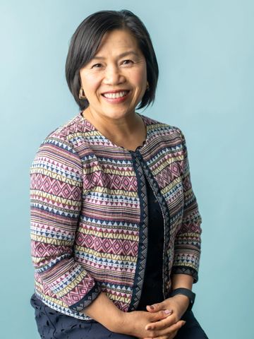 Smiling woman wearing a patterned jacket against a light blue background.