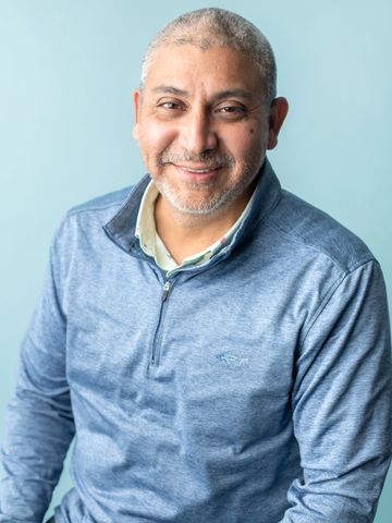 Smiling man in a blue quarter-zip sweater against a light blue background.