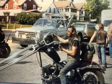 Man sitting on a custom chopper motorcycle in a residential neighborhood.