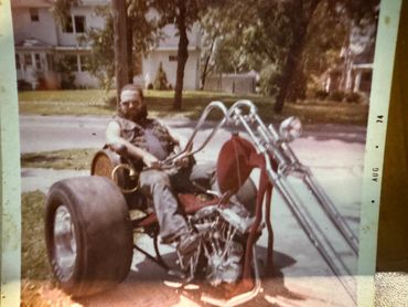 Man with beard sitting on a custom trike motorcycle with wide rear tires.