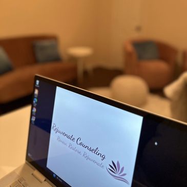 Laptop screen displaying Rejuvenate Counseling logo in a cozy room.