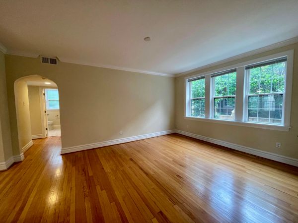 Empty room with wooden floors and large windows letting in natural light.