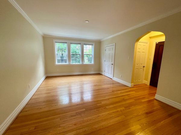 Empty room with hardwood floors and large windows letting in natural light.
