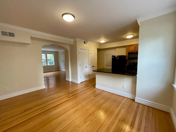 Empty living space with hardwood floors and kitchen area.