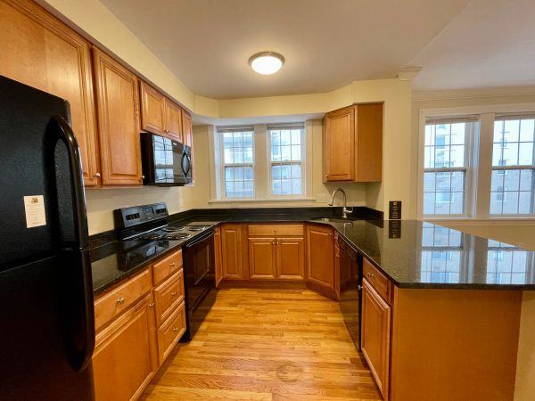 Modern kitchen with wooden cabinets and black appliances under warm lighting.