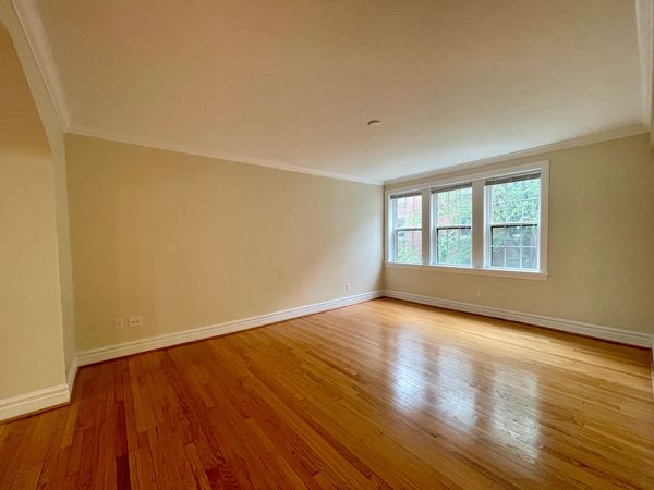 Empty room with wooden floors and large windows letting in natural light.