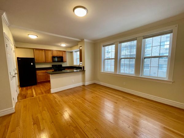 Empty apartment with hardwood floors and an open kitchen layout.