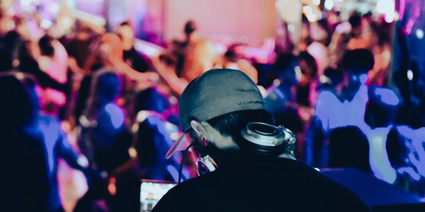 DJ performing with blurred crowd in vibrant lighting at a party.