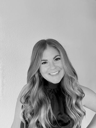 Black-and-white portrait of a smiling woman with long wavy hair against a plain background.
