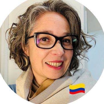 Smiling woman with glasses and curly hair wrapped in a beige scarf.