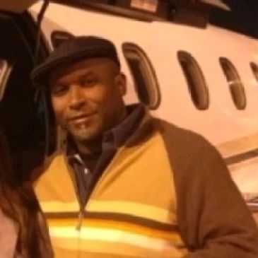 Man in a hat and striped sweater standing by a private jet.