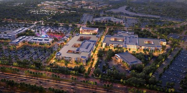 Aerial view of a well-lit urban complex at dusk with roads and parking lots.