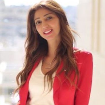 Smiling woman wearing a red blazer indoors with soft natural light.