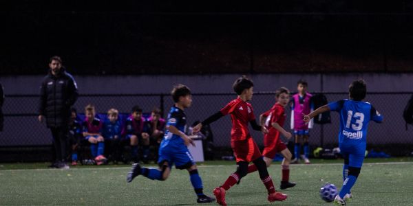 Kids playing soccer at night on a field.