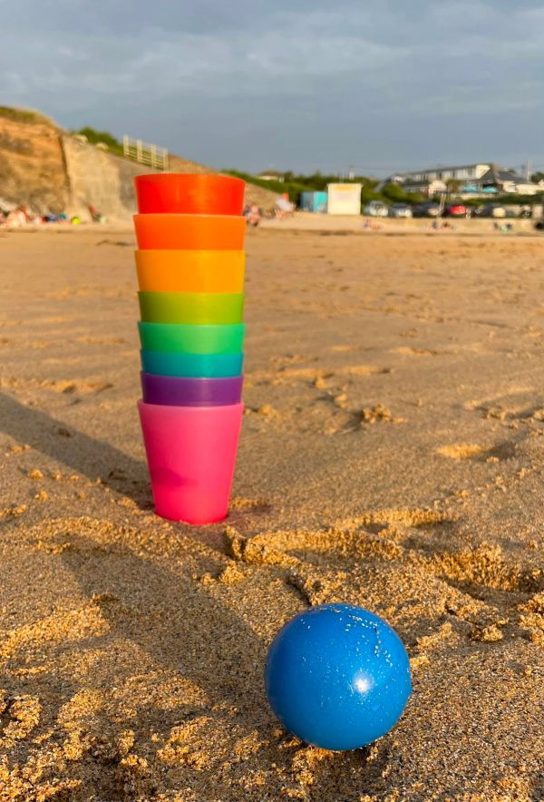 Stacked colorful cups and a blue ball on the beach sand.