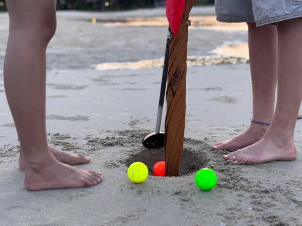 Children playing beach golf with colorful balls and clubs.