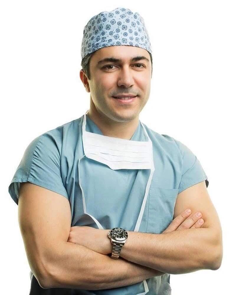 Smiling male surgeon in scrubs with arms crossed.