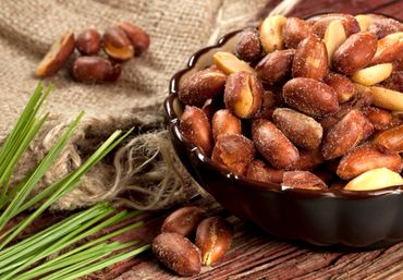 A bowl of roasted peanuts with some spilled on a wooden surface.