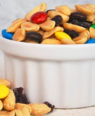 A bowl of trail mix with peanuts, raisins, and colorful candy-coated chocolates.