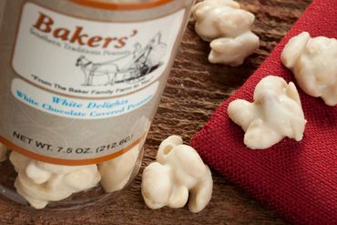 White chocolate covered popcorn spilling from a Bakers container onto a wooden surface.